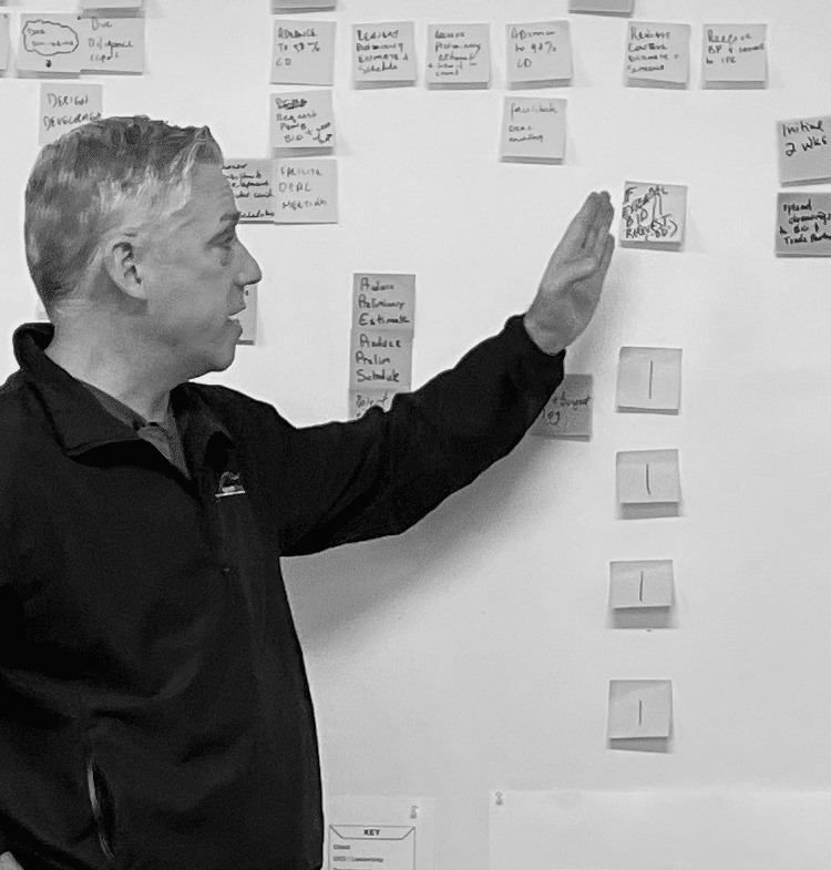 Fractional CFO helping to process map, pointing to sticky notes on white board.